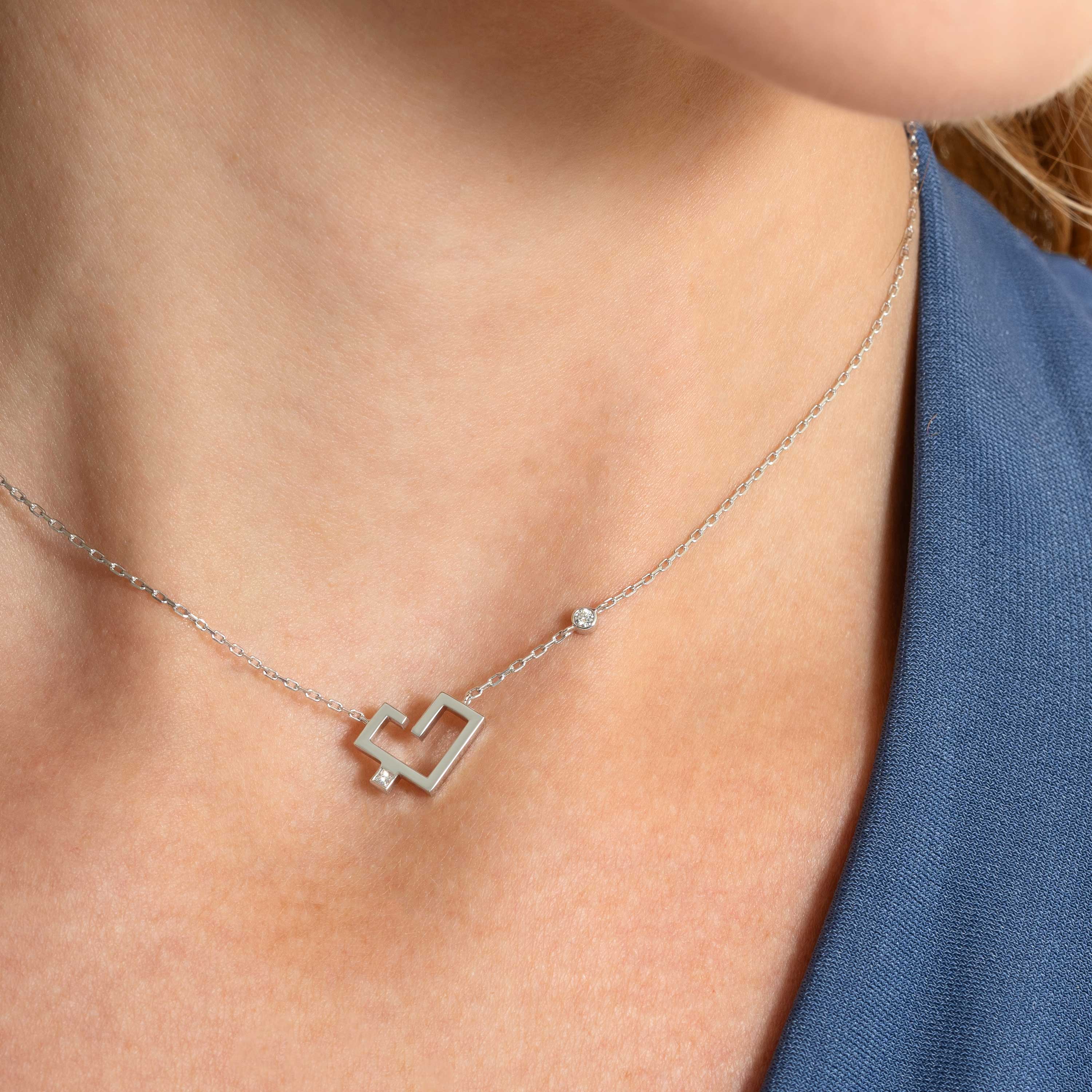 A silver-toned necklace with a heart-shaped pendant and solitaire accent rests against a neck beside a blue garment.