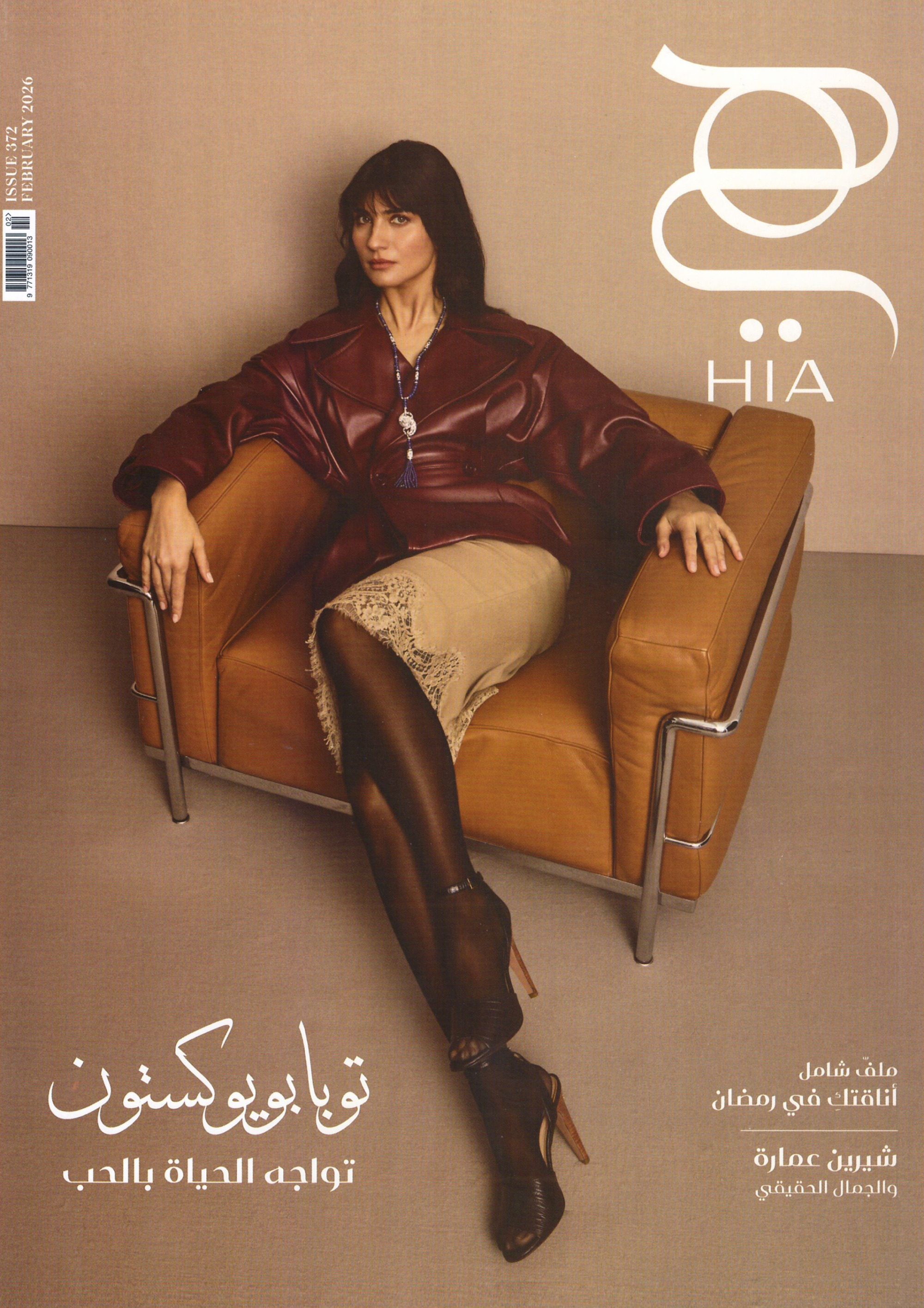 A dark-haired model reclines in a burgundy leather coat and beige skirt on a tan chair for HIA Magazine's Key of Love issue.