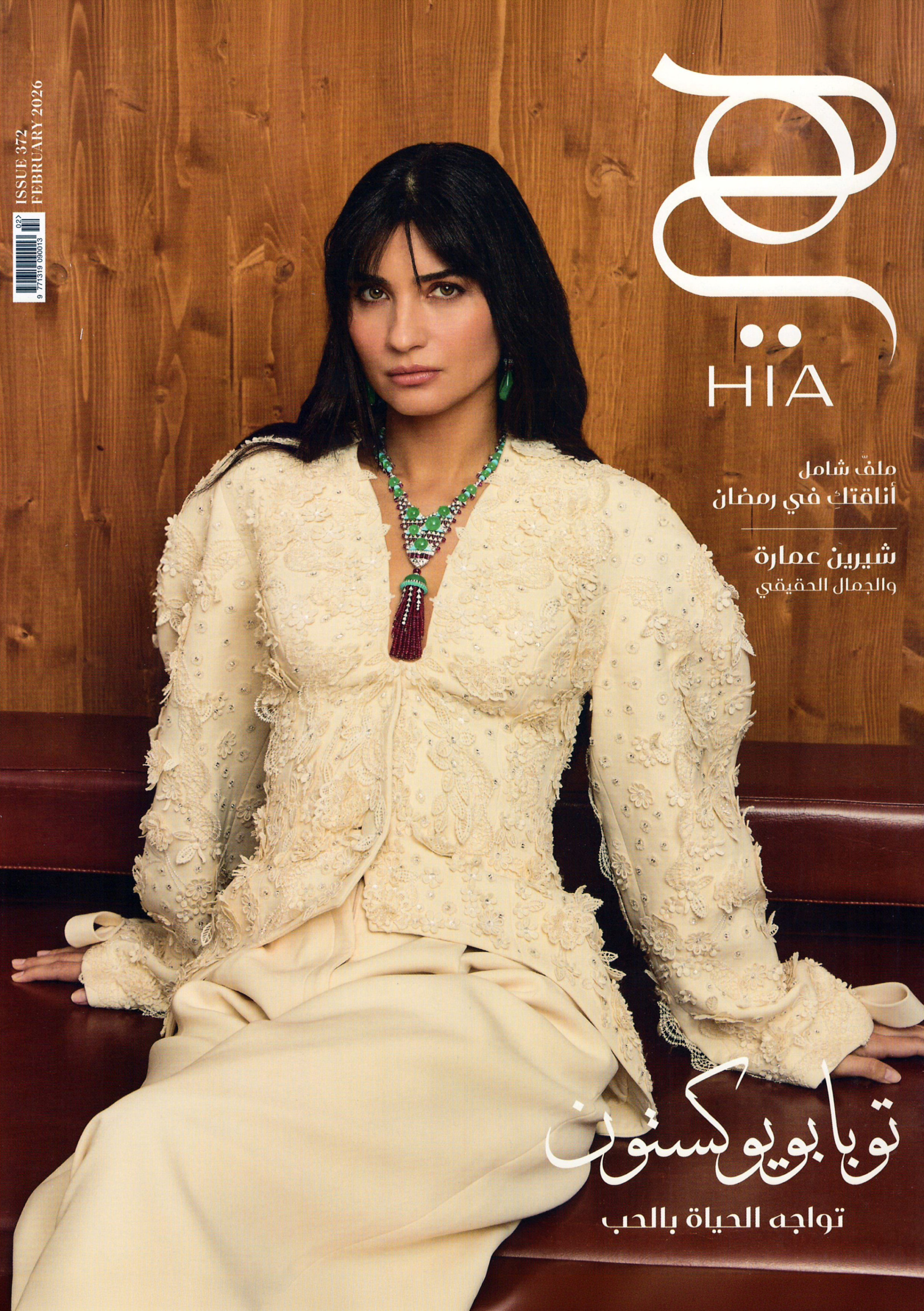 A Hia Magazine cover shows a model in an ivory embroidered outfit wearing a layered green necklace and sitting against a wood backdrop.