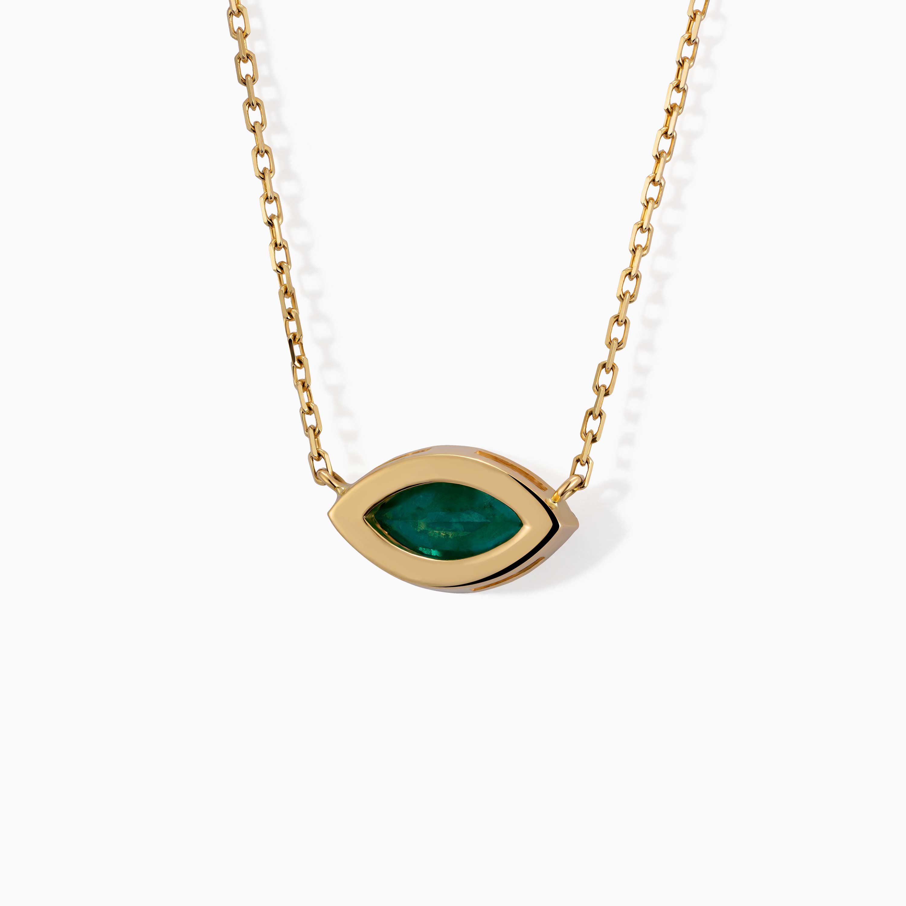 A gold chain necklace holds an eye-shaped green emerald pendant with a polished marquise frame on white.