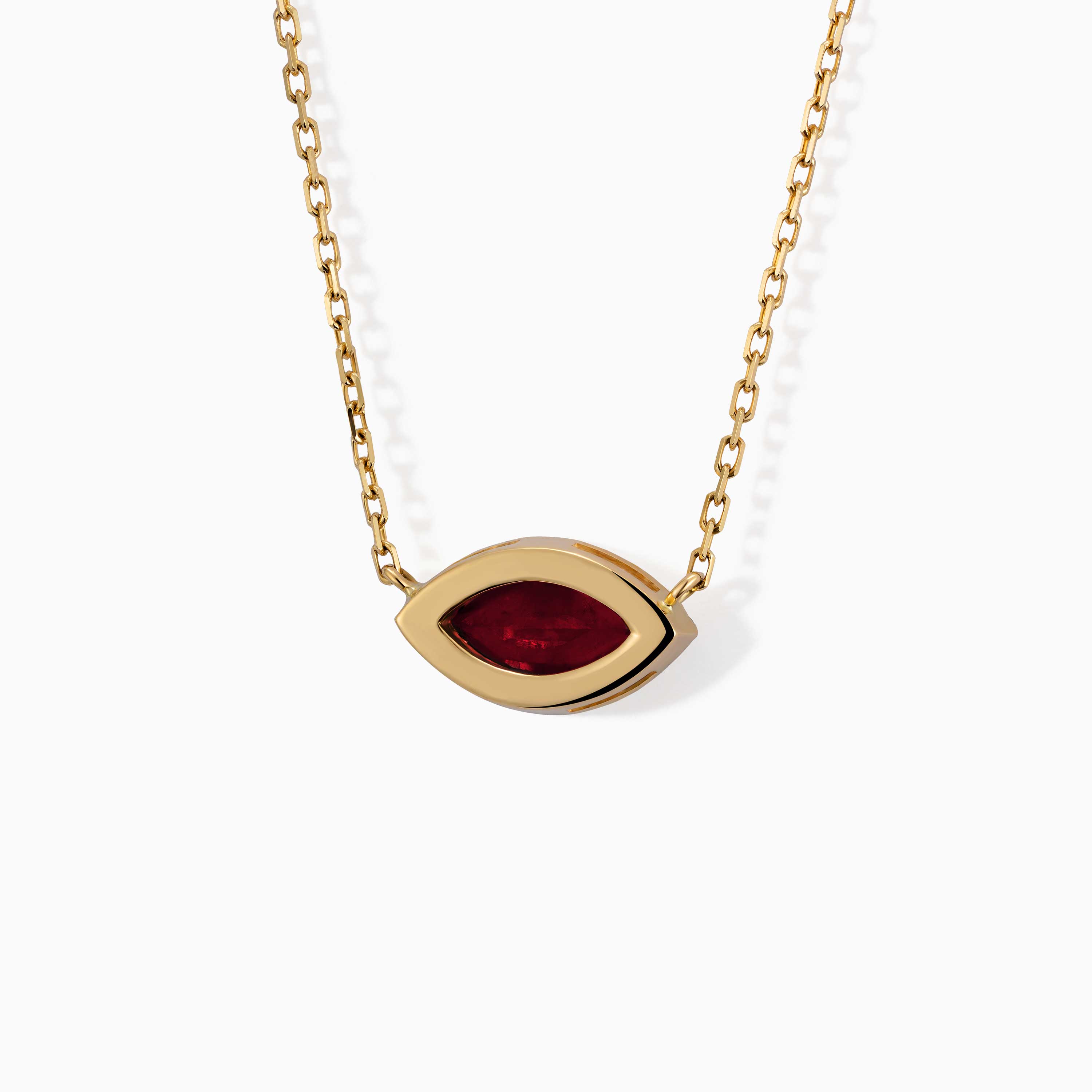 A gold chain necklace with a marquise-shaped red gemstone pendant from The Eye rests on a white background.