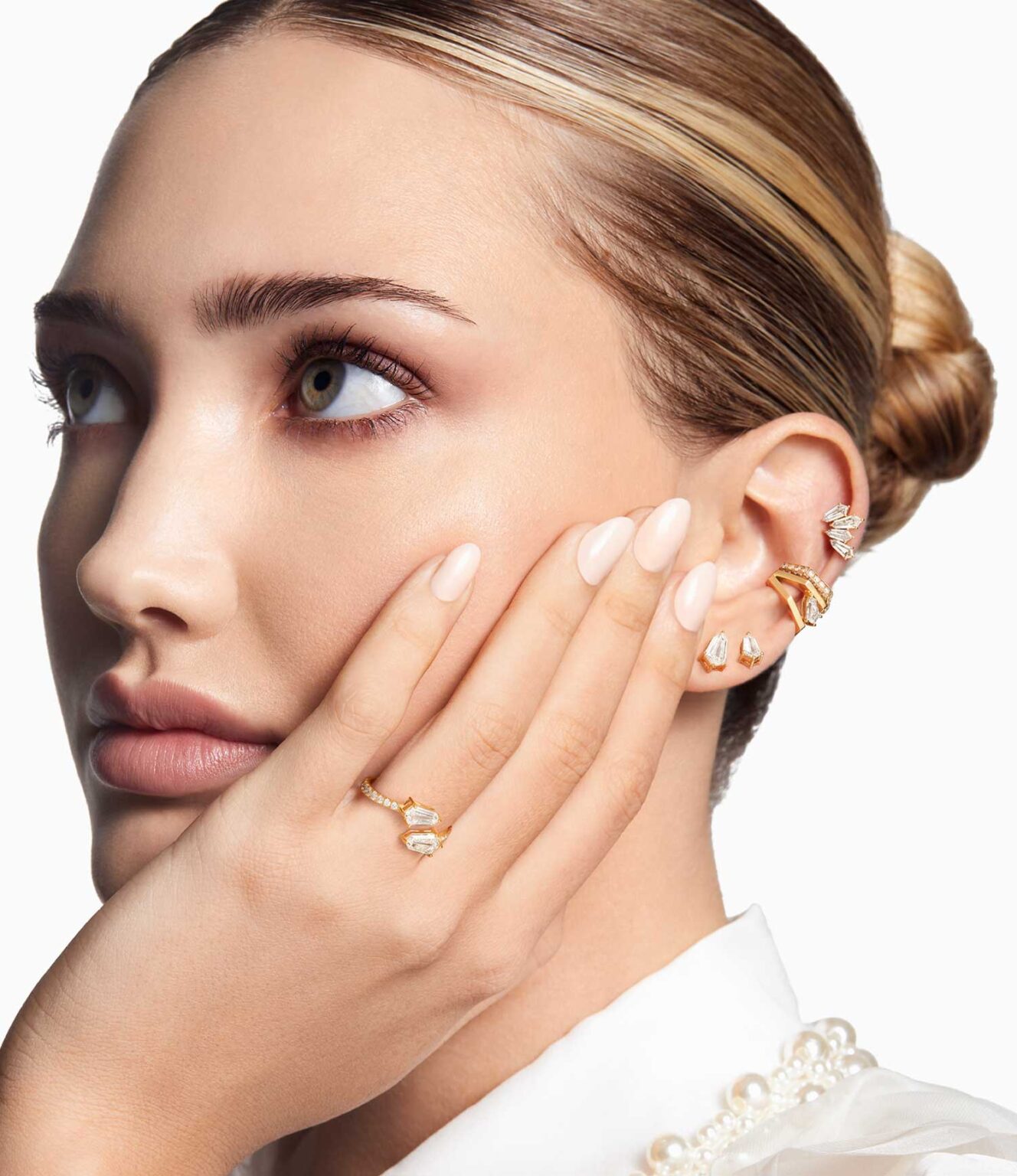 Close view of lotus_mobile style gold jewelry, including sparkle rings and earrings, with manicured hands near the face on a clean background.