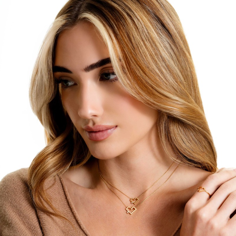 A woman with blonde hair wears layered gold Hubb necklaces and a matching geometric ring against a white background.