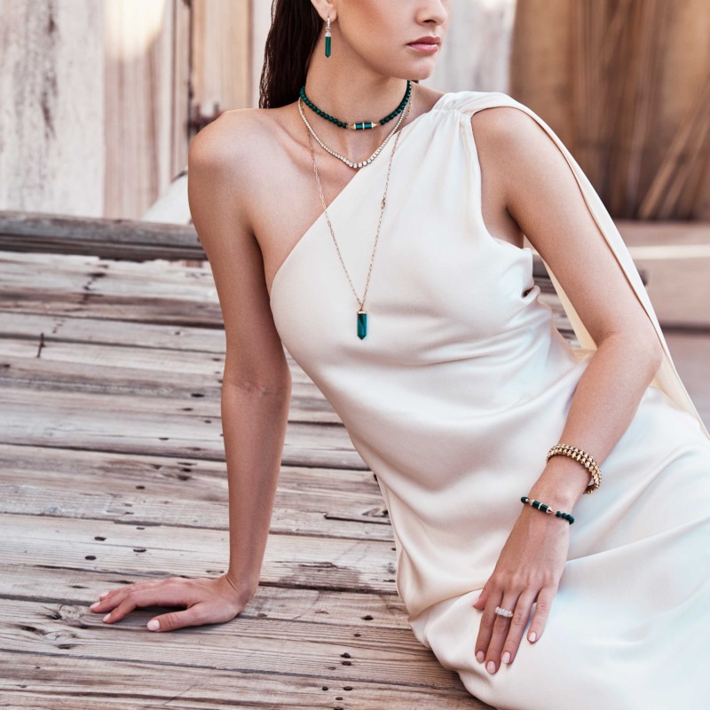 Chakra Graduated Gold Cuff by Yataghan Jewellery styled with layered gold necklaces, green gemstone details and a white draped dress.