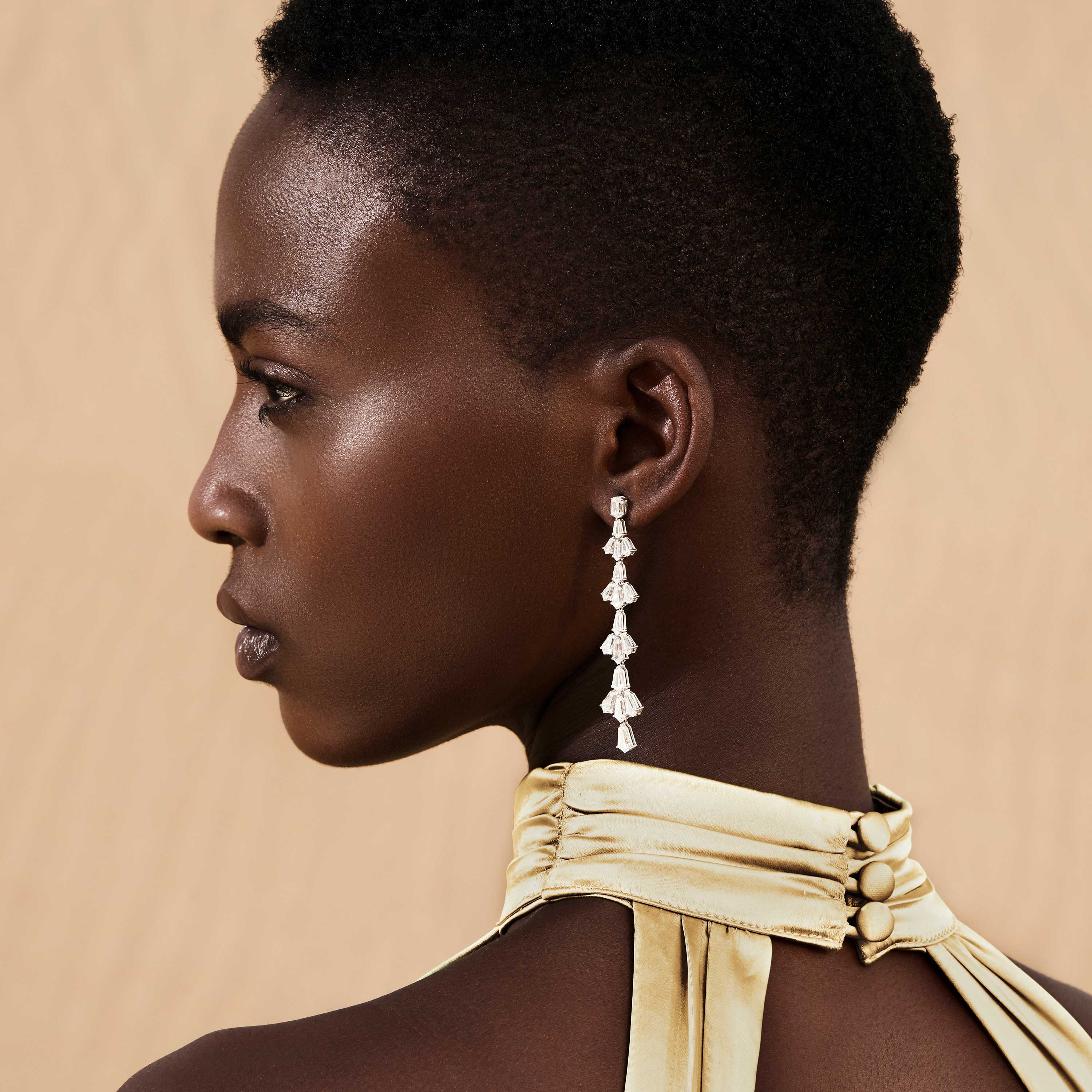 Lotus Evening Earrings by Yataghan Jewellery with dangling lotus charms in silver tones, shown near the ear against a warm beige background.