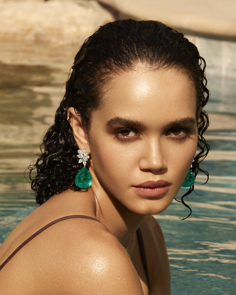 A model wears emerald teardrop earrings with diamond floral settings, reflecting Yataghan High Jewellery craftsmanship and refined gemstone artistry.