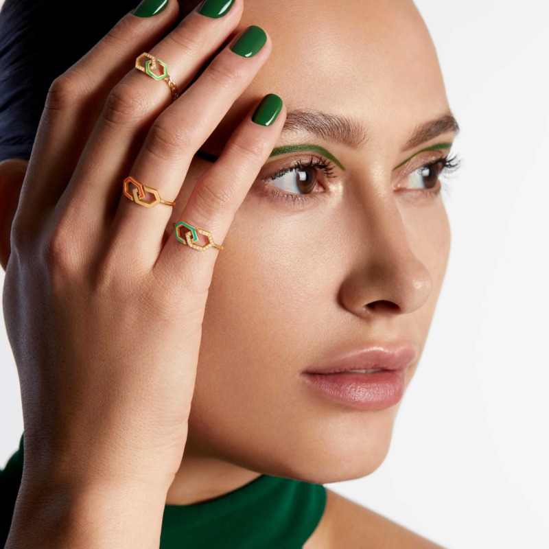 A close-up of a model wearing Infinity Enamel Gold Ring Band rings with green enamel and gold detailing, framing the face with matching emerald nails.