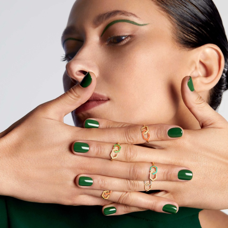 A close-up model poses with gold infinity enamel diamond rings, green nail polish, and matching green eye accents against a soft light background.