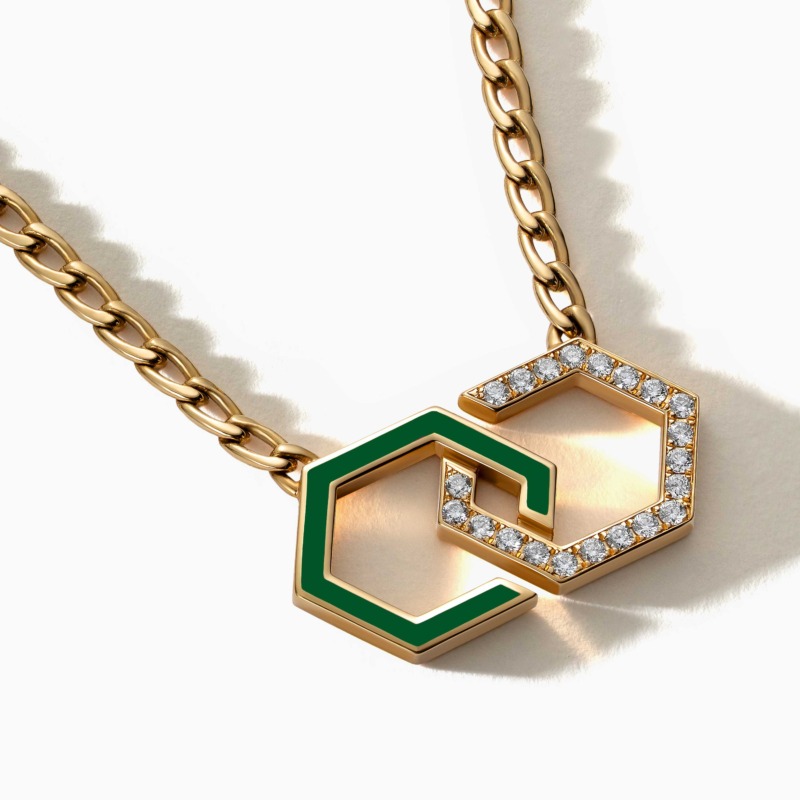 A gold chain necklace with green enamel infinity links and diamond accents rests on a white background, reflecting the Infinity Enamel Unchained design.