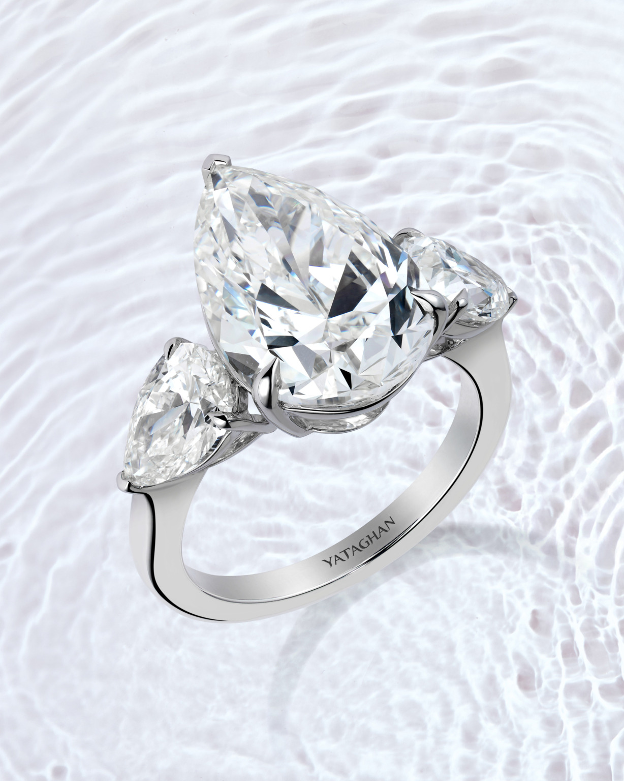 An Yataghan engagement ring showcases a pear-cut diamond center stone with two matching side diamonds in a polished platinum setting.
