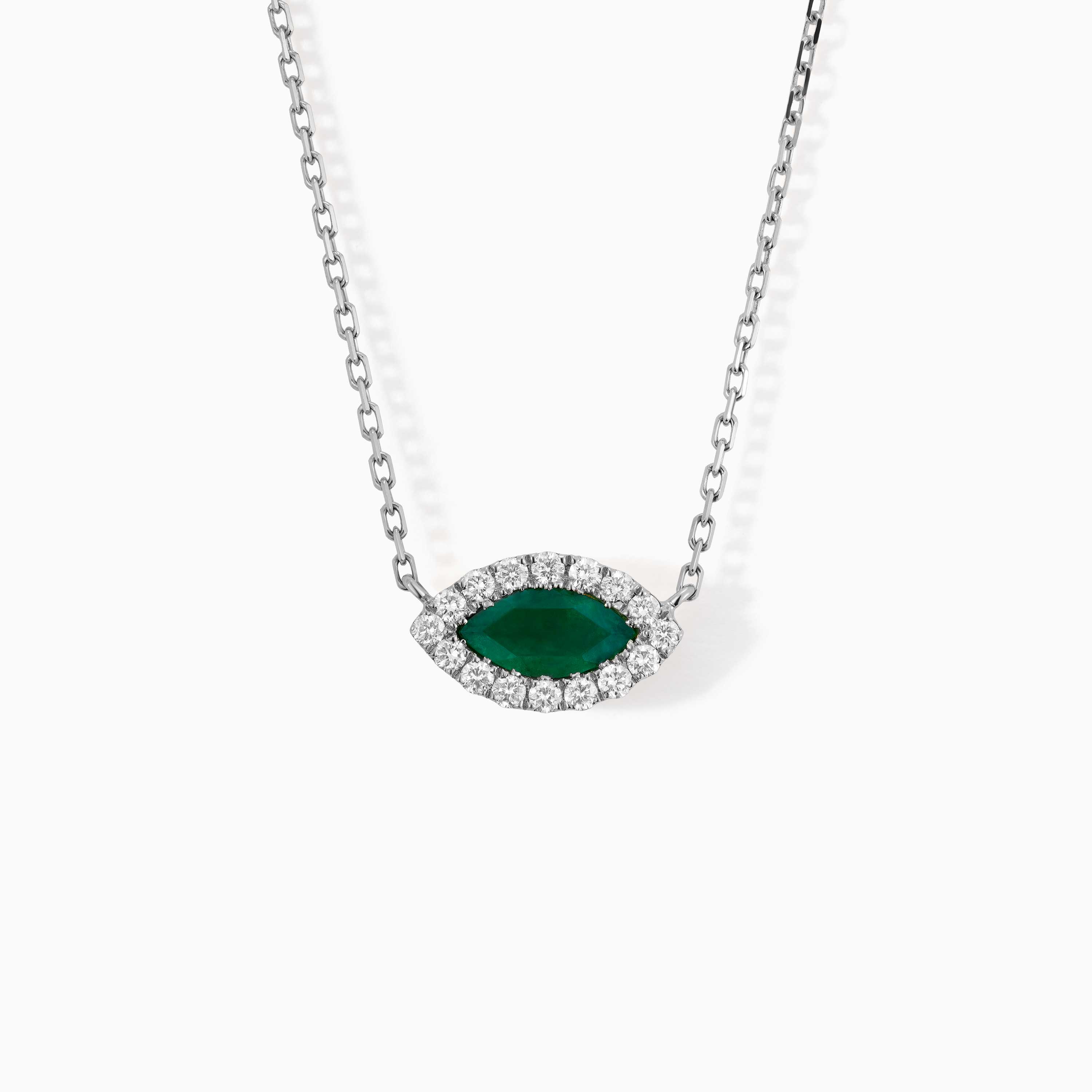 A marquise emerald pendant surrounded by diamonds hangs from a white gold chain on a plain white background.