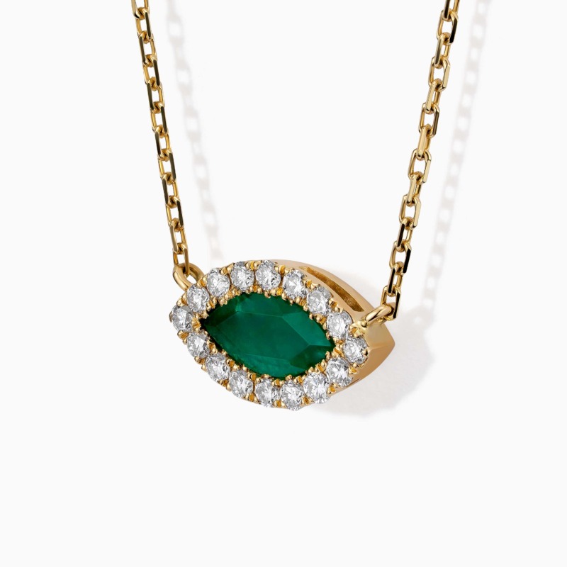 An emerald marquise pendant framed by diamonds hangs from a yellow gold chain on a white background.