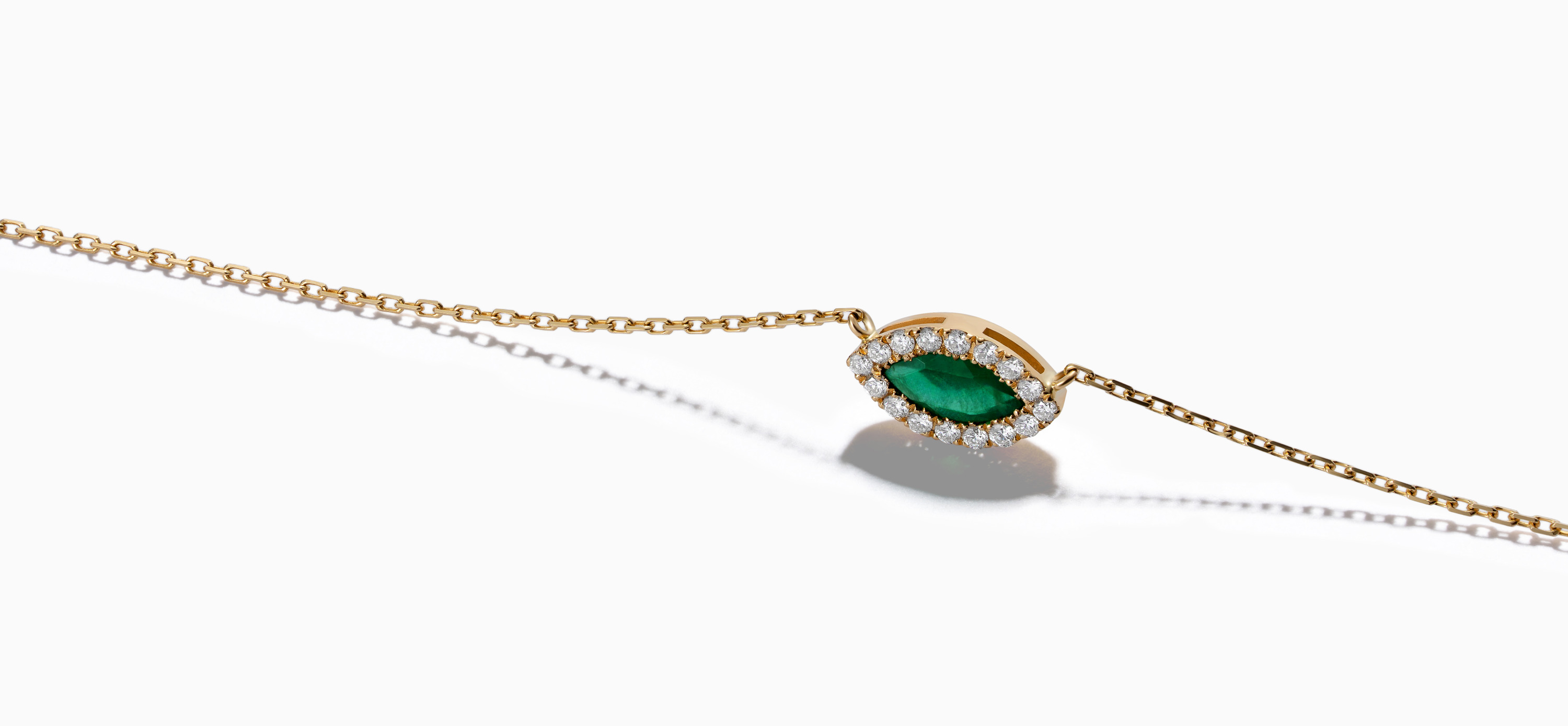 A gold Eye collection necklace centers on a green marquise gemstone, framed by small diamonds on a white background.